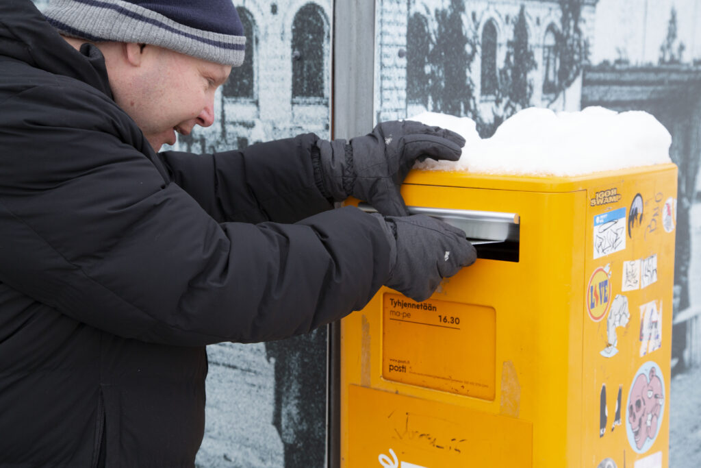 Henkilö laittaa kirjeen postilaatikkoon